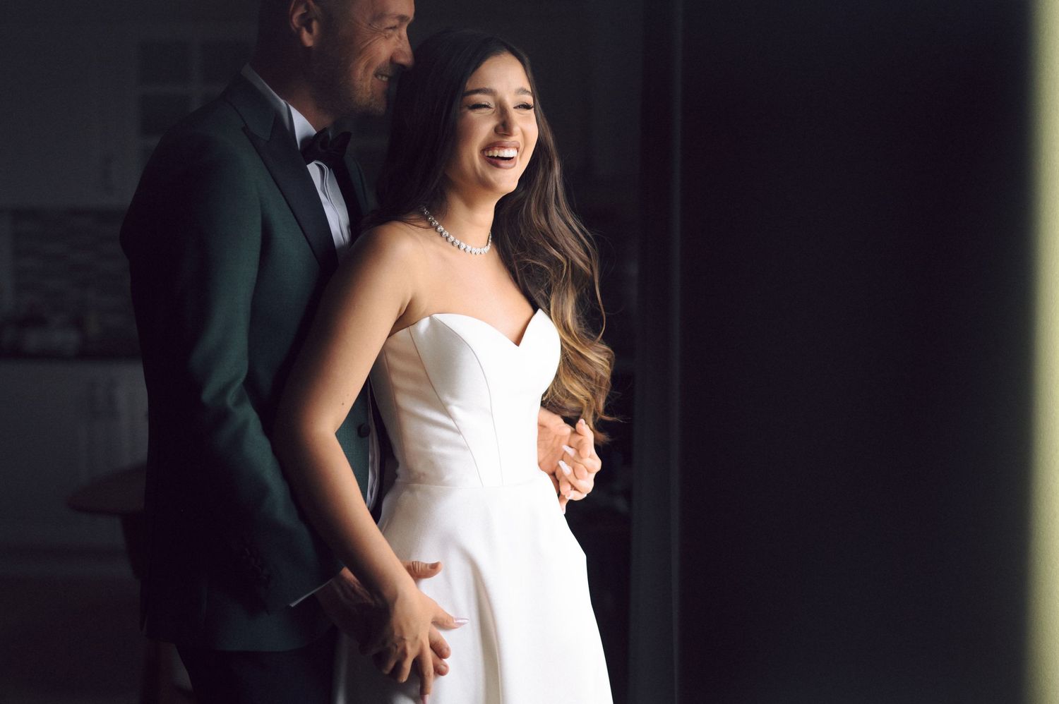 A couple sharing a candid laughing moment together, with the woman wearing an elegant white strapless gown.