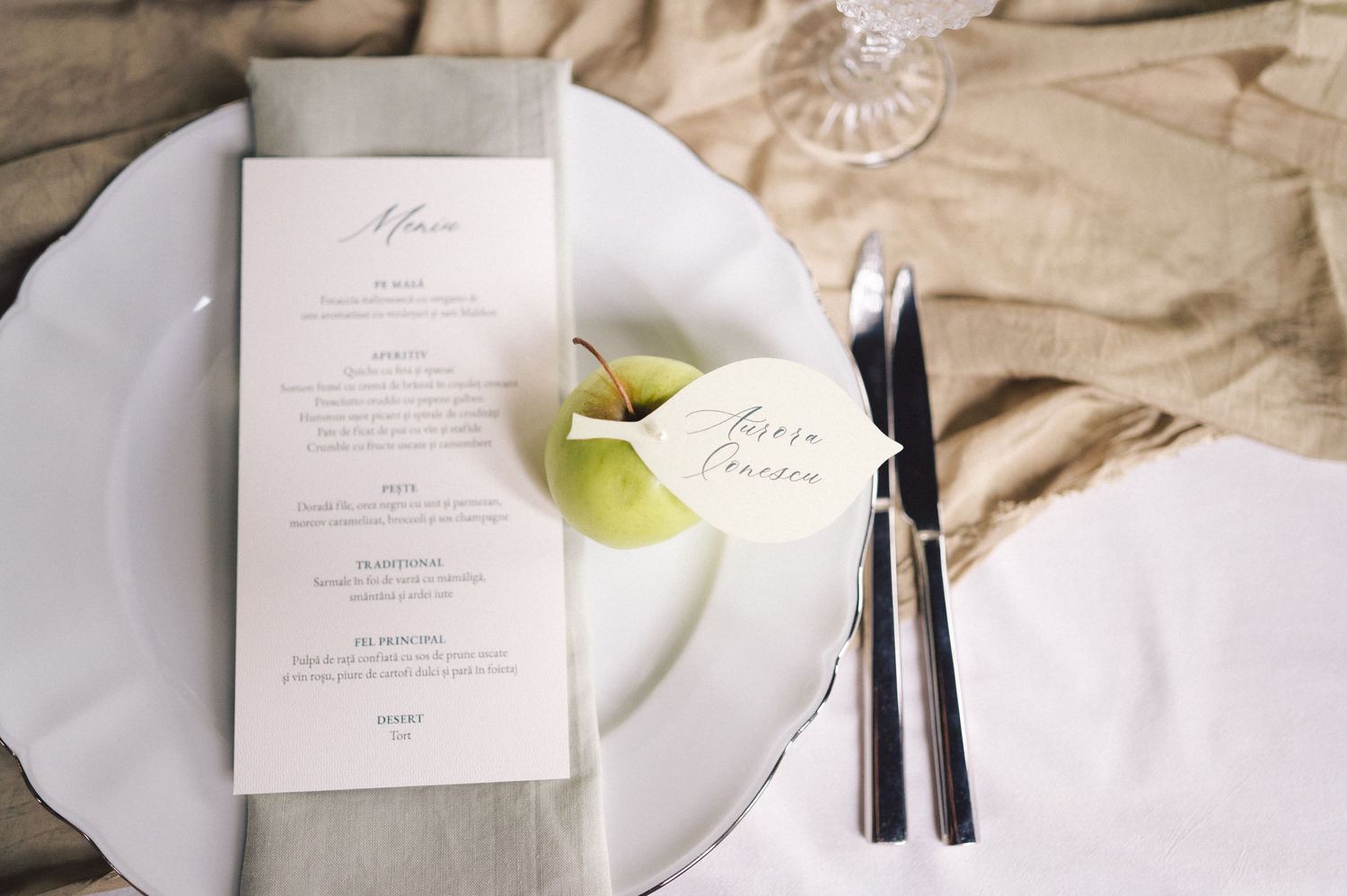 Elegant wedding reception place setting with menu card and place card in white and gold accents on light tablecloth.