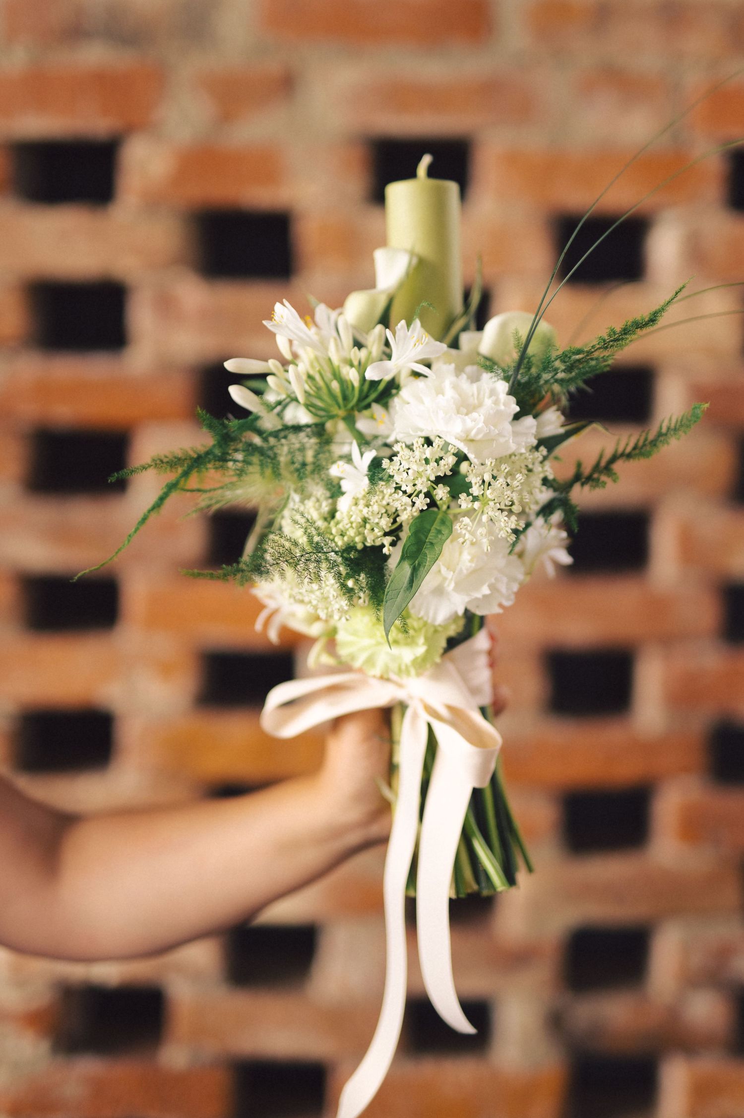 A delicate white floral wedding boutonniere with ribbon on display against a rustic brick background.