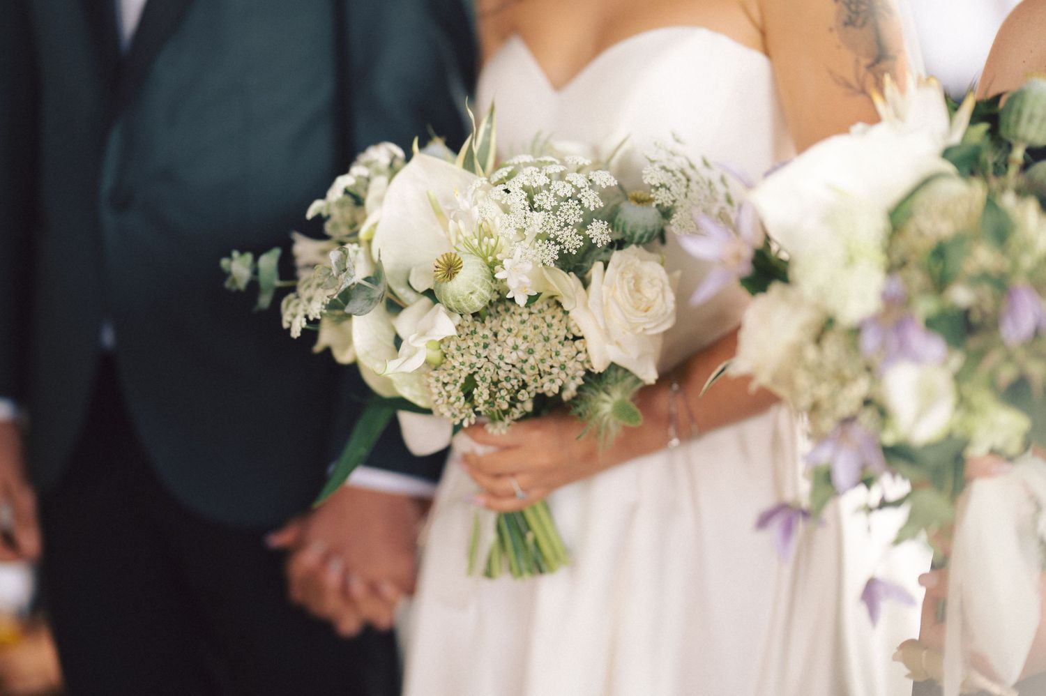 Close-up of elegant white and green wedding bouquet with roses and baby's breath held at a formal ceremony.