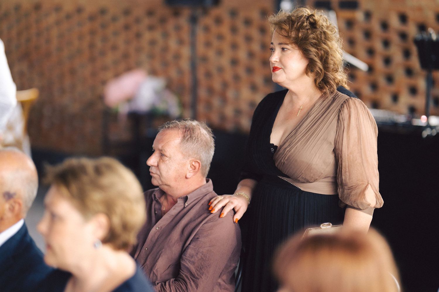 Audience members seated at an event are shown watching attentively with focused expressions.