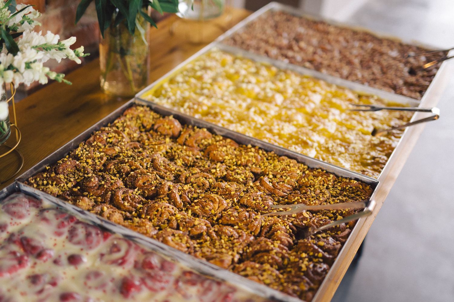 Overhead view of three different gourmet pasta dishes served in buffet-style metal trays.