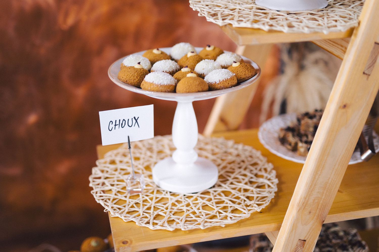 Small pastries displayed on a white pedestal cake stand with a delicate lace pattern on a rustic wooden dessert table.
