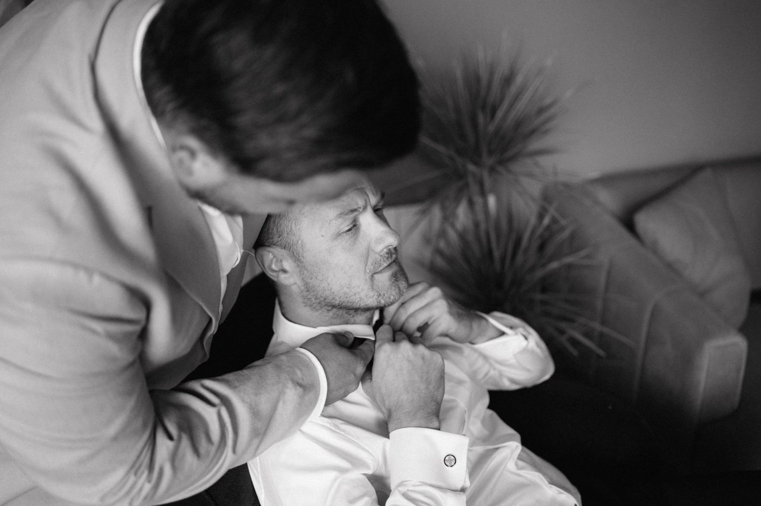 Two people share an intimate black and white moment on a couch as one leans down towards the other.