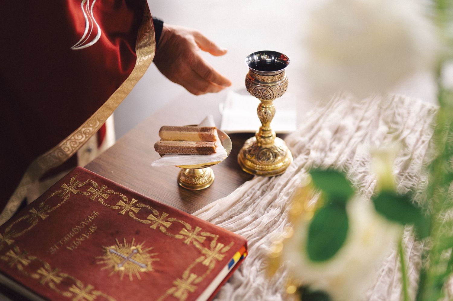 A chalice and holy book arranged on a lace tablecloth during a sacred religious ceremony.