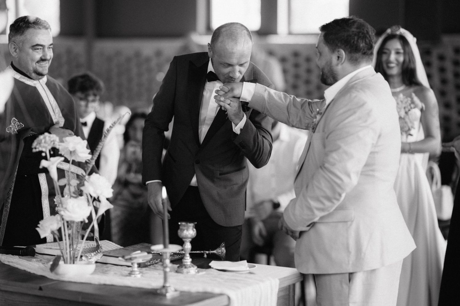 A black and white photo of guests celebrating at an elegant gathering with drinks and laughter around a table.