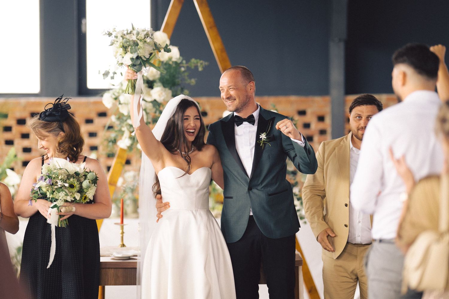A celebratory moment at a modern indoor wedding ceremony with elegant white decor and flowers.