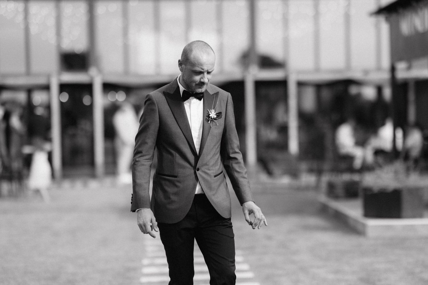 A black and white photo showing a person in a formal suit walking outdoors at an event venue.