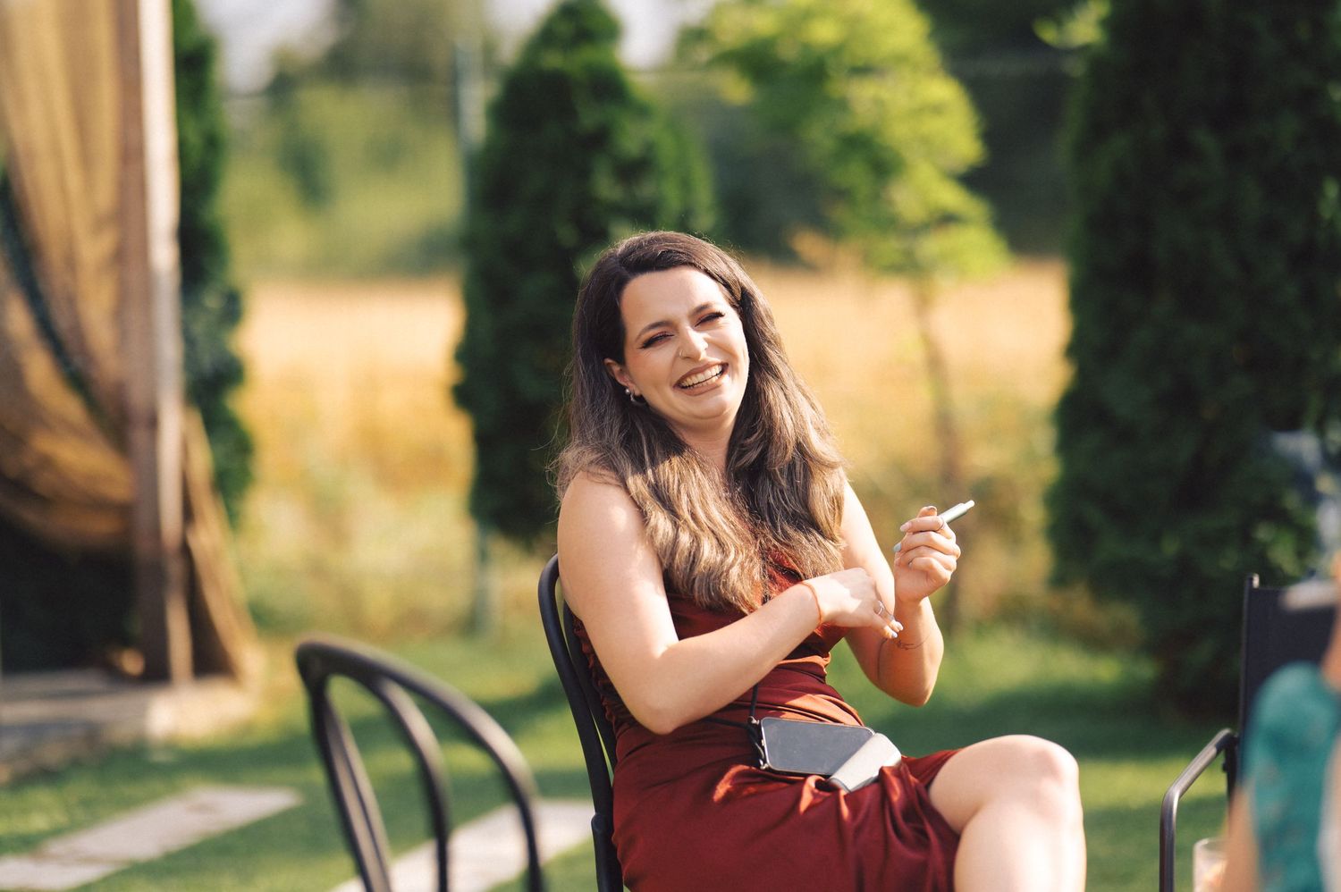 Woman in red dress sits outdoors on sunny day using mobile phone in garden setting.