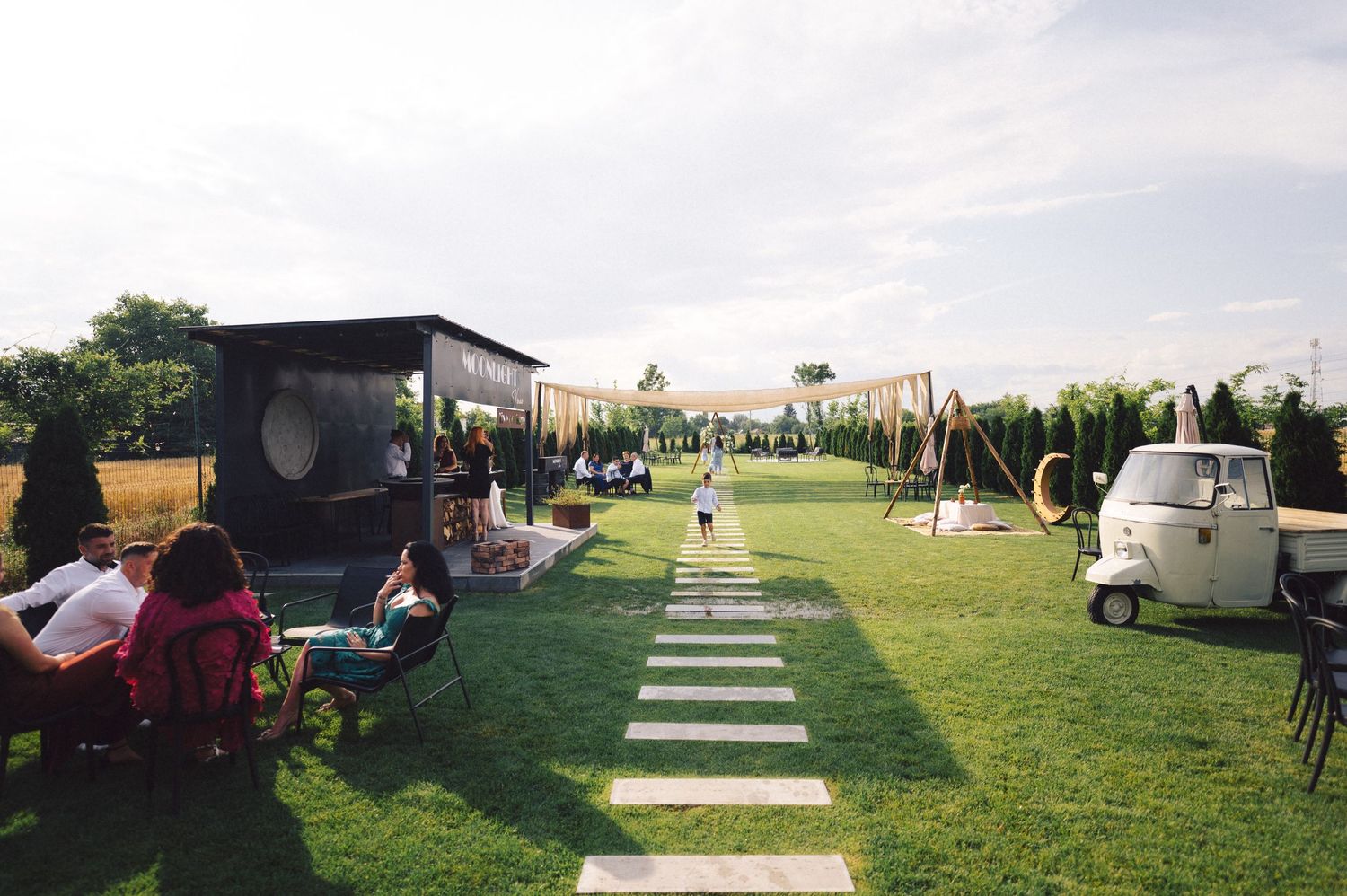Outdoor event space with food trucks and lawn seating on a grassy area with stone pathway under cloudy skies.