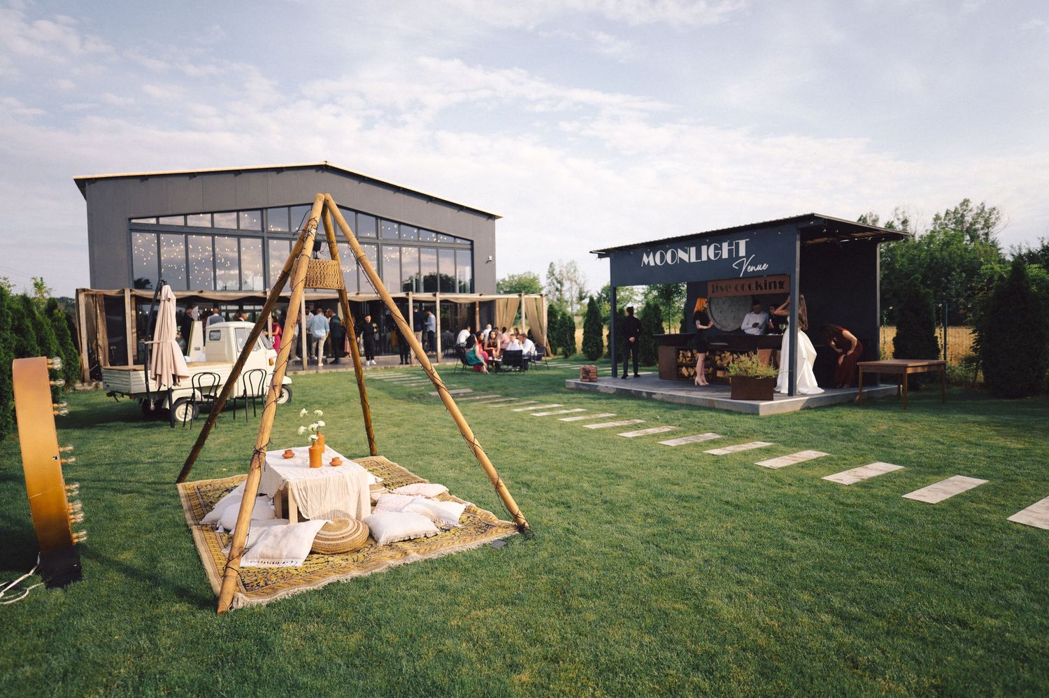 Modern outdoor garden venue with wooden swing set and lounge area on a manicured lawn under cloudy skies.