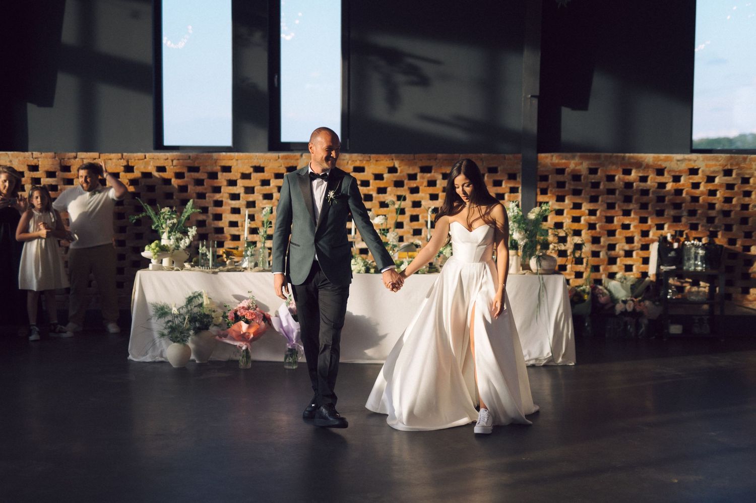 A couple shares their first dance at a modern wedding reception with geometric wall decor and floral arrangements.