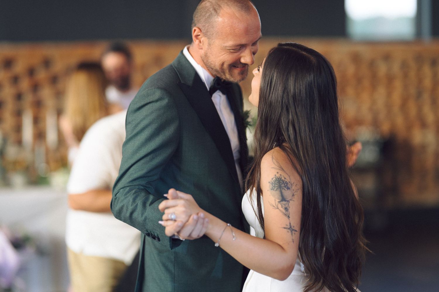 A couple shares their first dance together at their wedding reception, with the groom wearing a forest green suit.