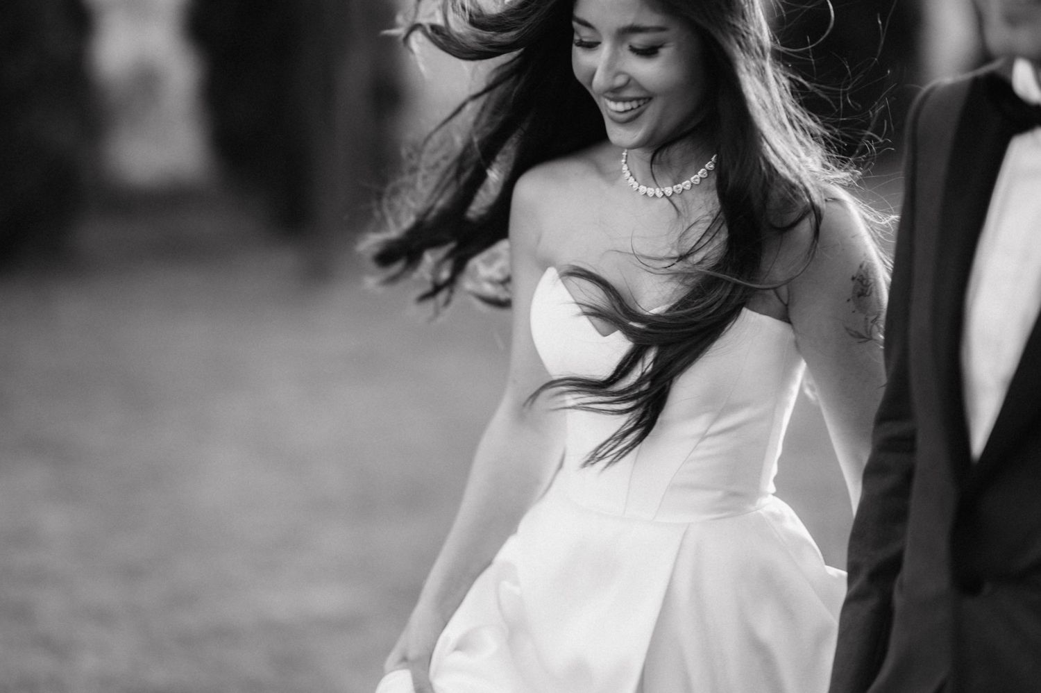 A joyful bride in a white wedding dress laughs and twirls on a cobblestone street in black and white photography.