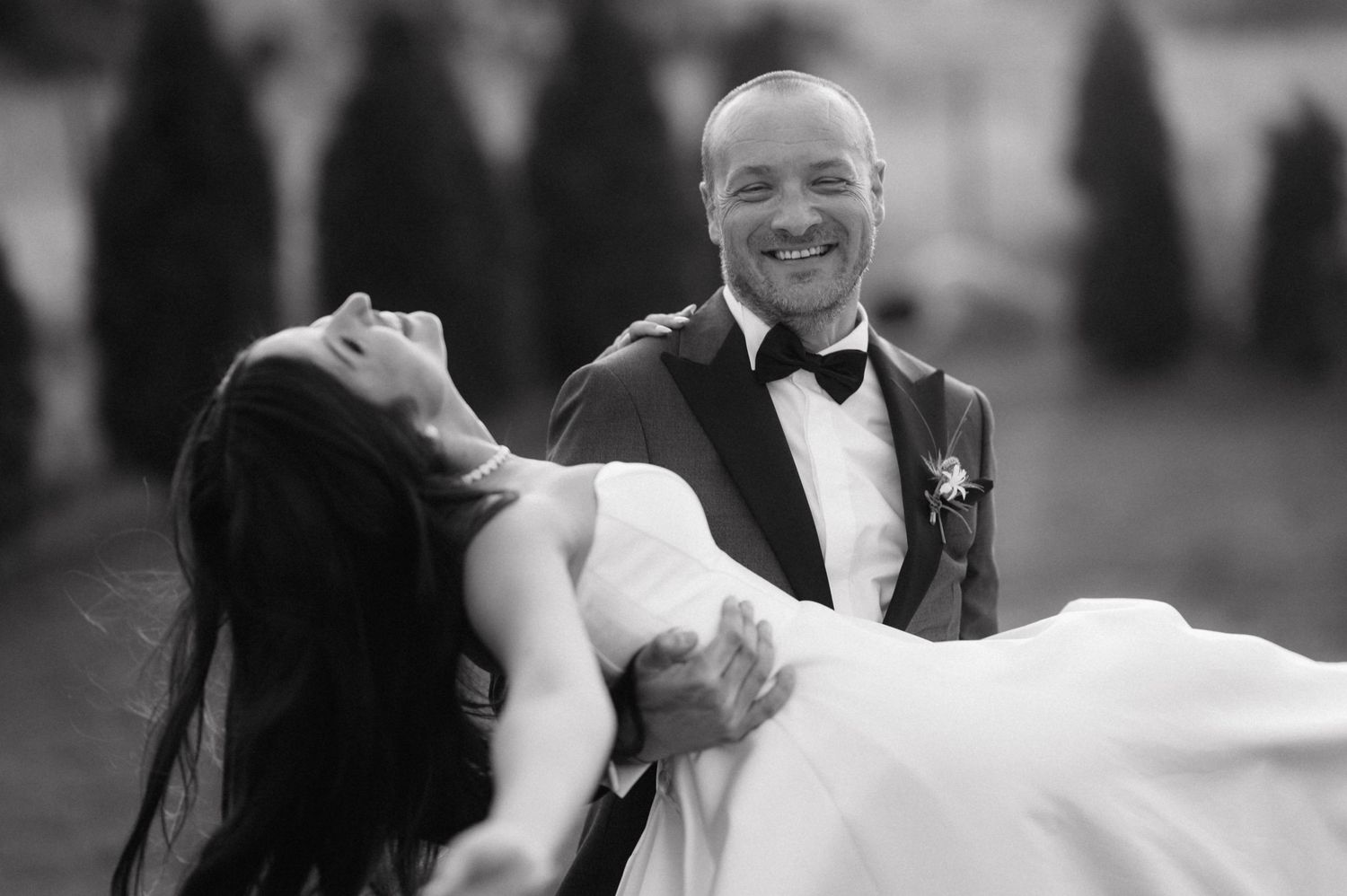 A joyful black and white wedding photograph showing a groom in a tuxedo holding his bride in a graceful dip.