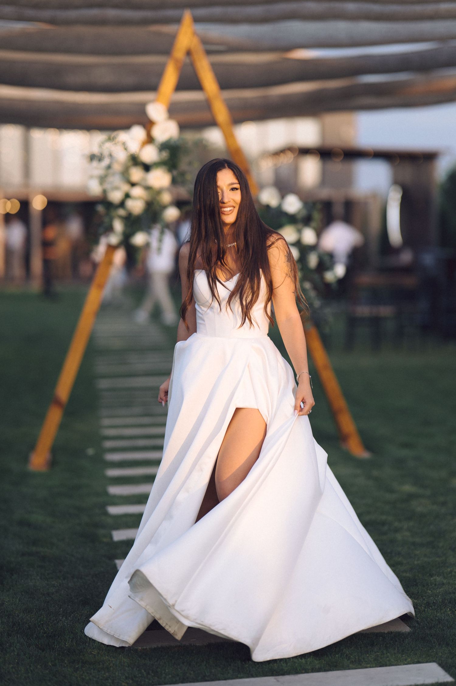 A person in a flowing white dress poses gracefully on a green lawn with yellow swing frames in the background.