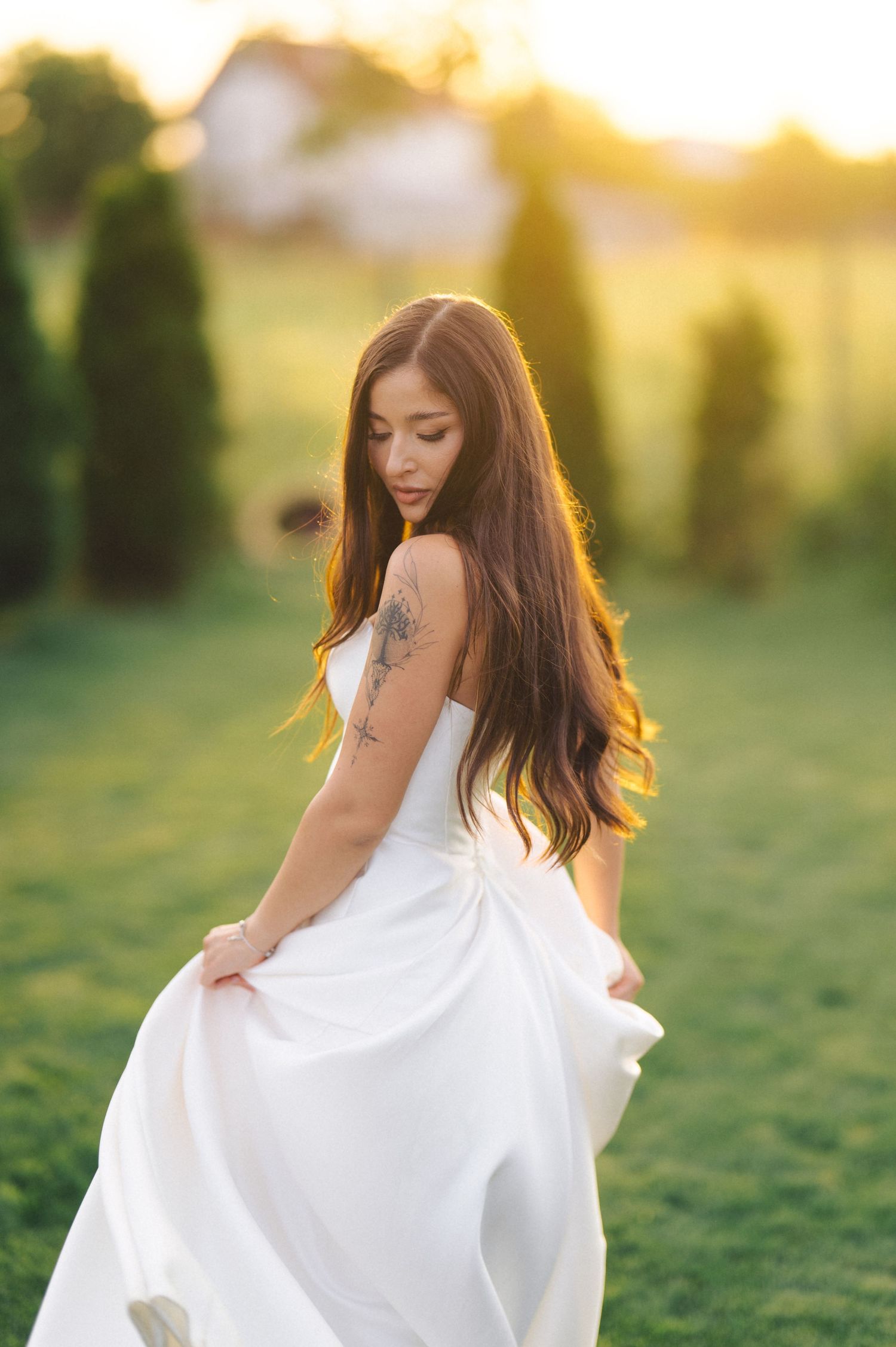 Ethereal outdoor portrait of a figure in a flowing white dress at sunset with glowing golden backlighting.