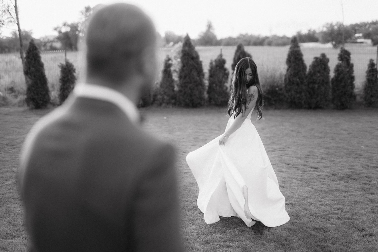 Wedding party members pose in a row outdoors at a scenic meadow location during a celebration.
