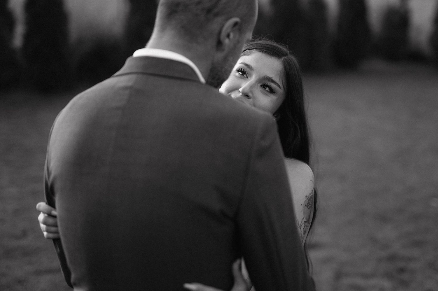 A nostalgic black and white photo shows a couple embracing in a tender romantic moment by the water.