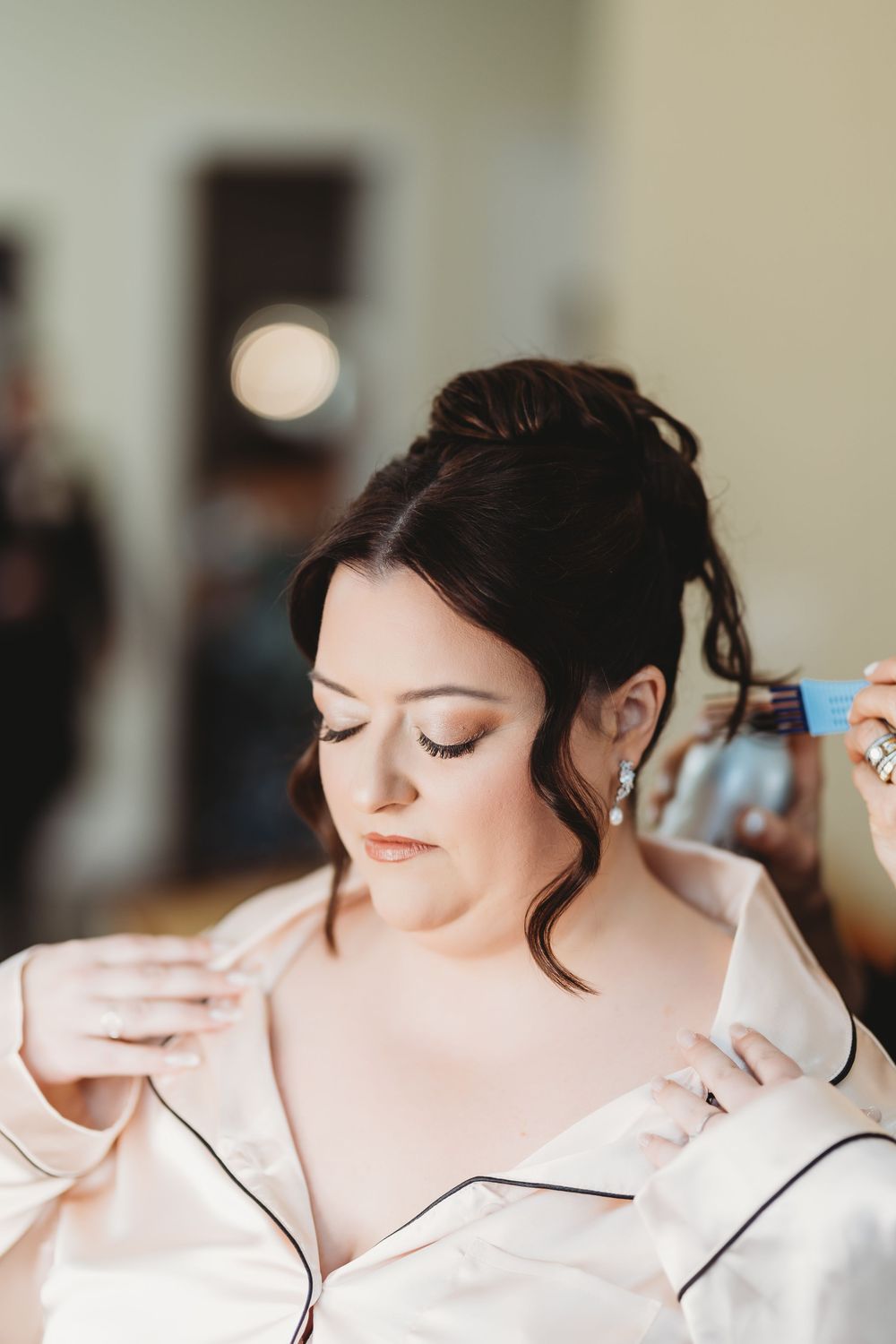 Someone getting their hair styled while wearing a white satin robe during wedding preparations.