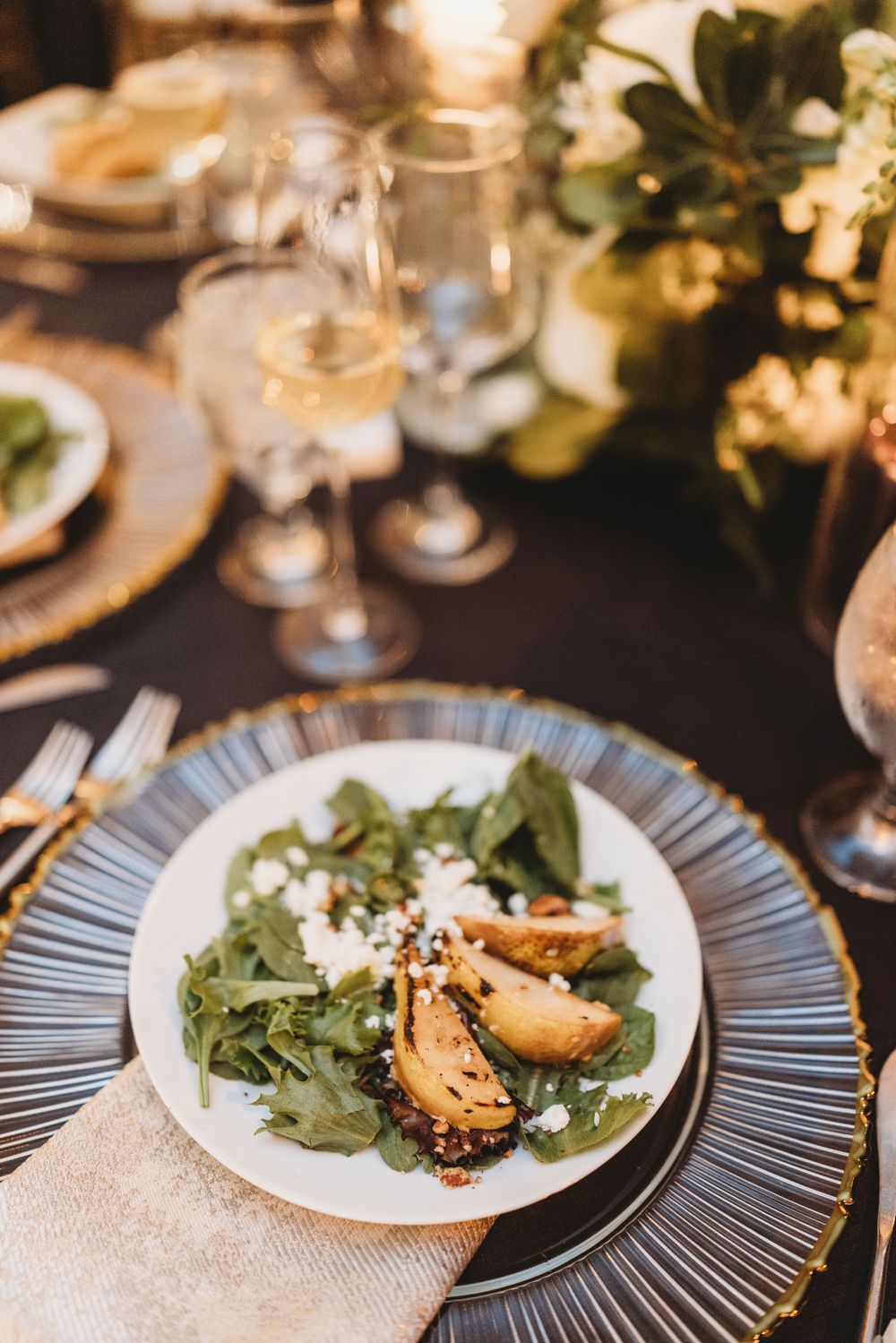 Elegant dinner plate with roasted pear salad garnished with arugula and goat cheese on a textured metallic charger.
