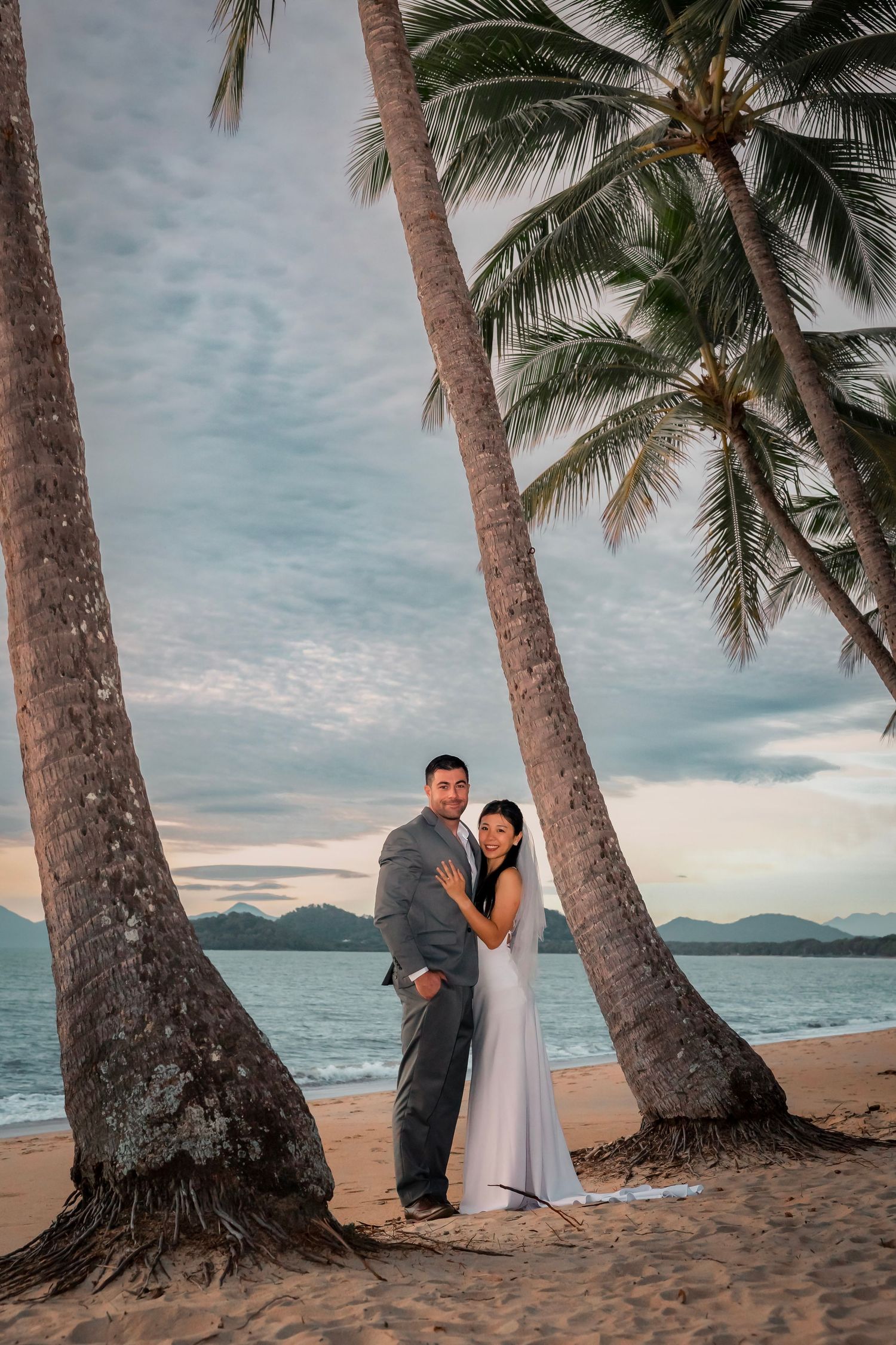 A romantic beach wedding photo series showing a couple embracing against a scenic coastal backdrop during sunset.