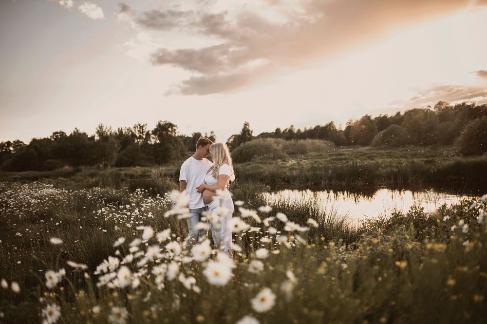 Romantic sunset photoshoot in a dreamy field of white daisies beside a reflective lake.