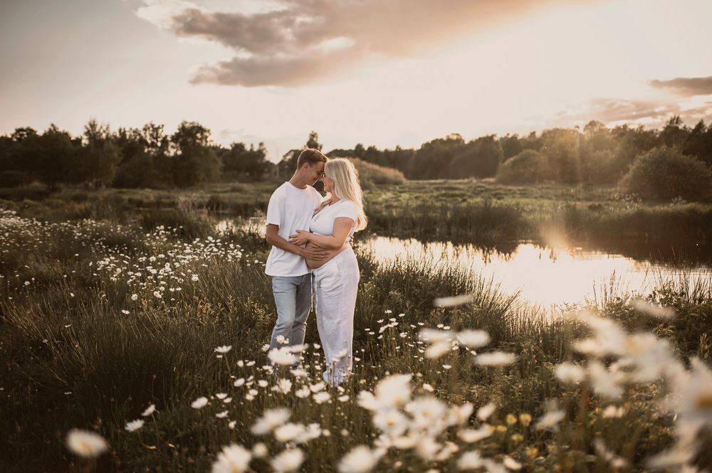 Golden hour maternity photos captured in a serene wildflower field beside a calm lake.