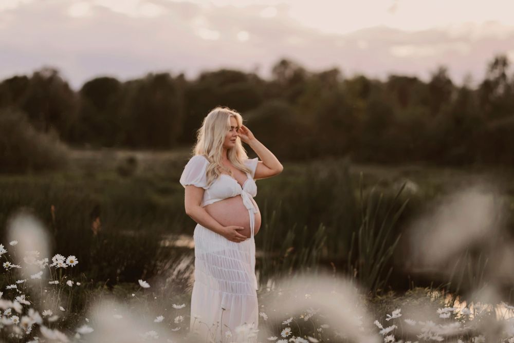 Romantic maternity photoshoot in a dreamy field of white wildflowers at sunset.