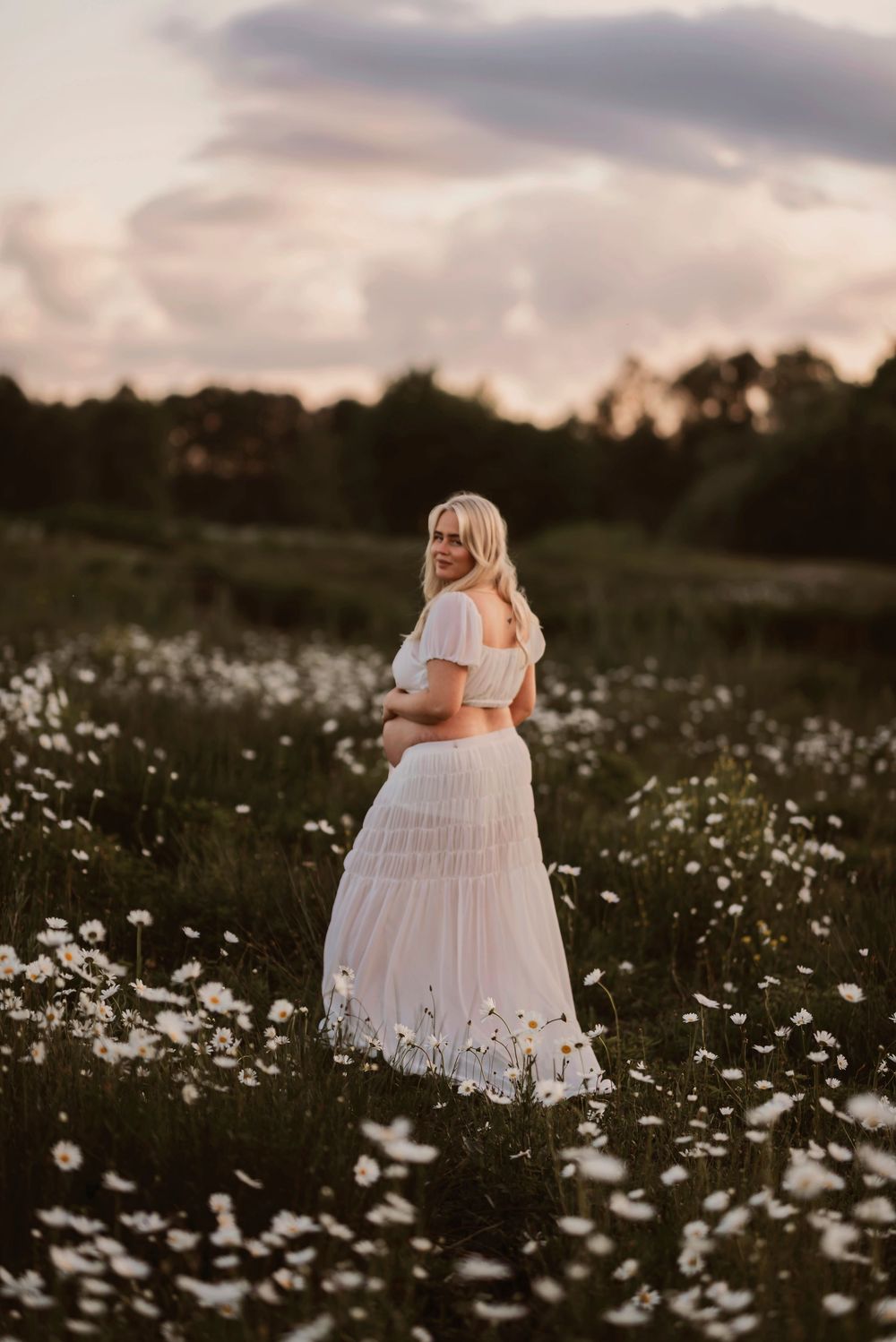 A white dress flows through a field of wild daisies at sunset creating a dreamy summer scene.