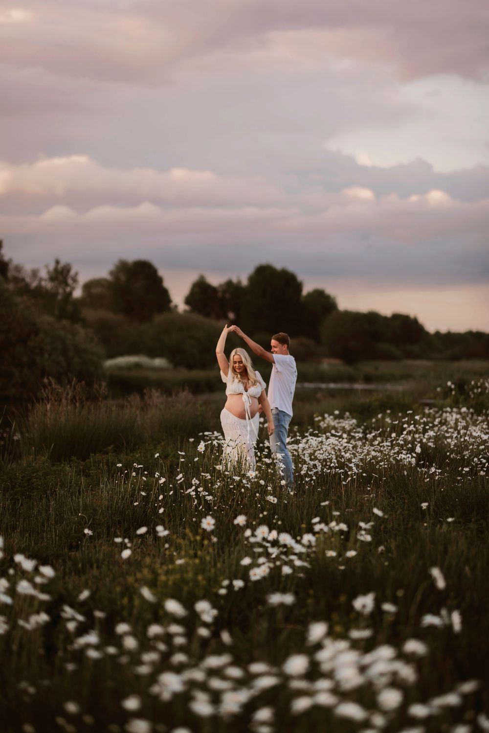 Couple dancing together in a dreamy meadow filled with white wildflowers at sunset.