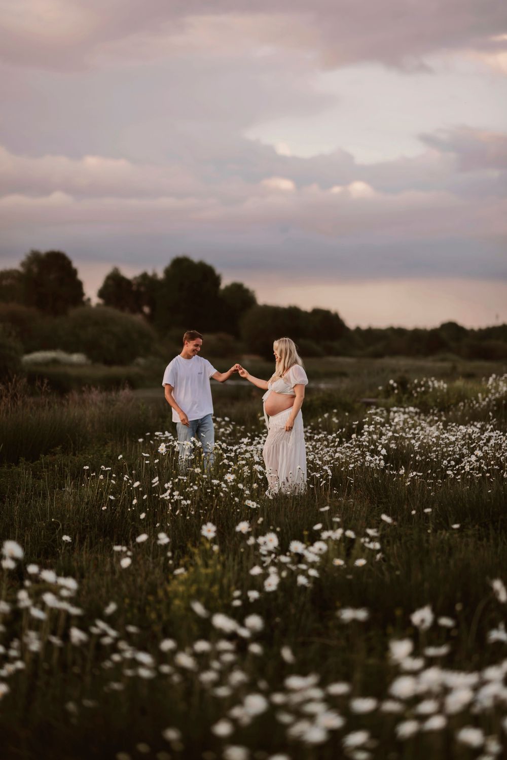Romantic scene of two people walking through a flowering field under moody evening skies.