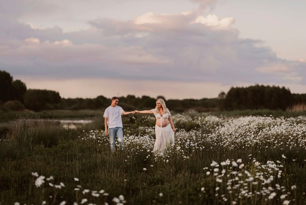 Ethereal panoramic view of a couple walking through a meadow filled with daisies at dusk.
