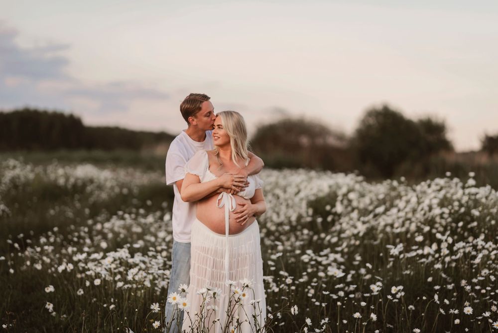 Intimate moment captured between a couple in a field of white daisies during golden hour.