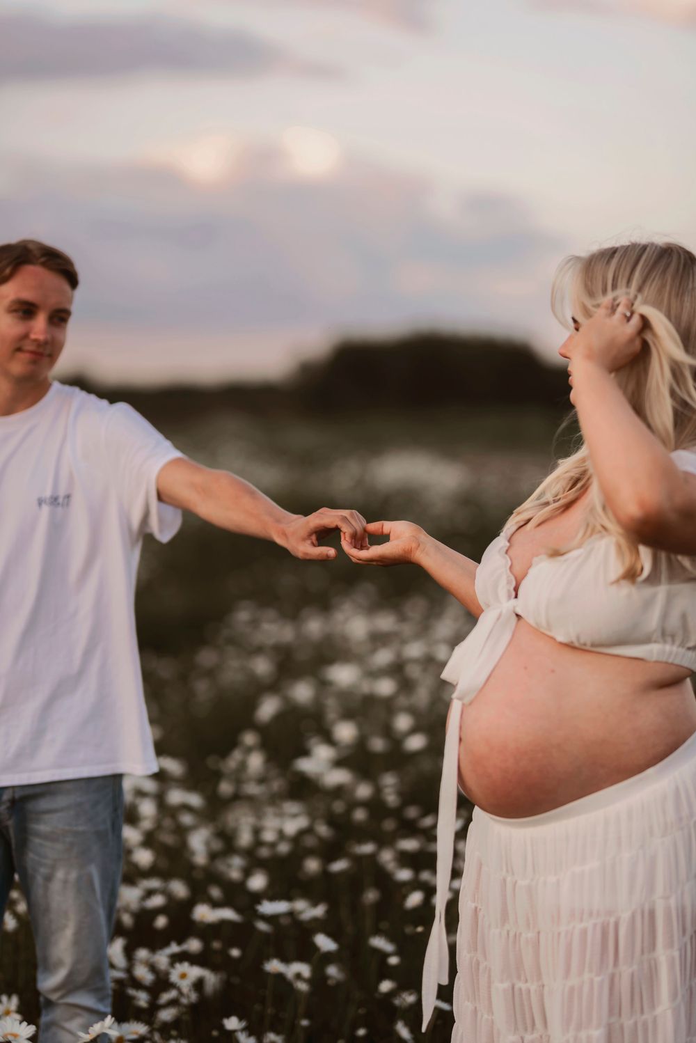 Intimate maternity moment captured in a daisy field during sunset with gentle natural lighting.