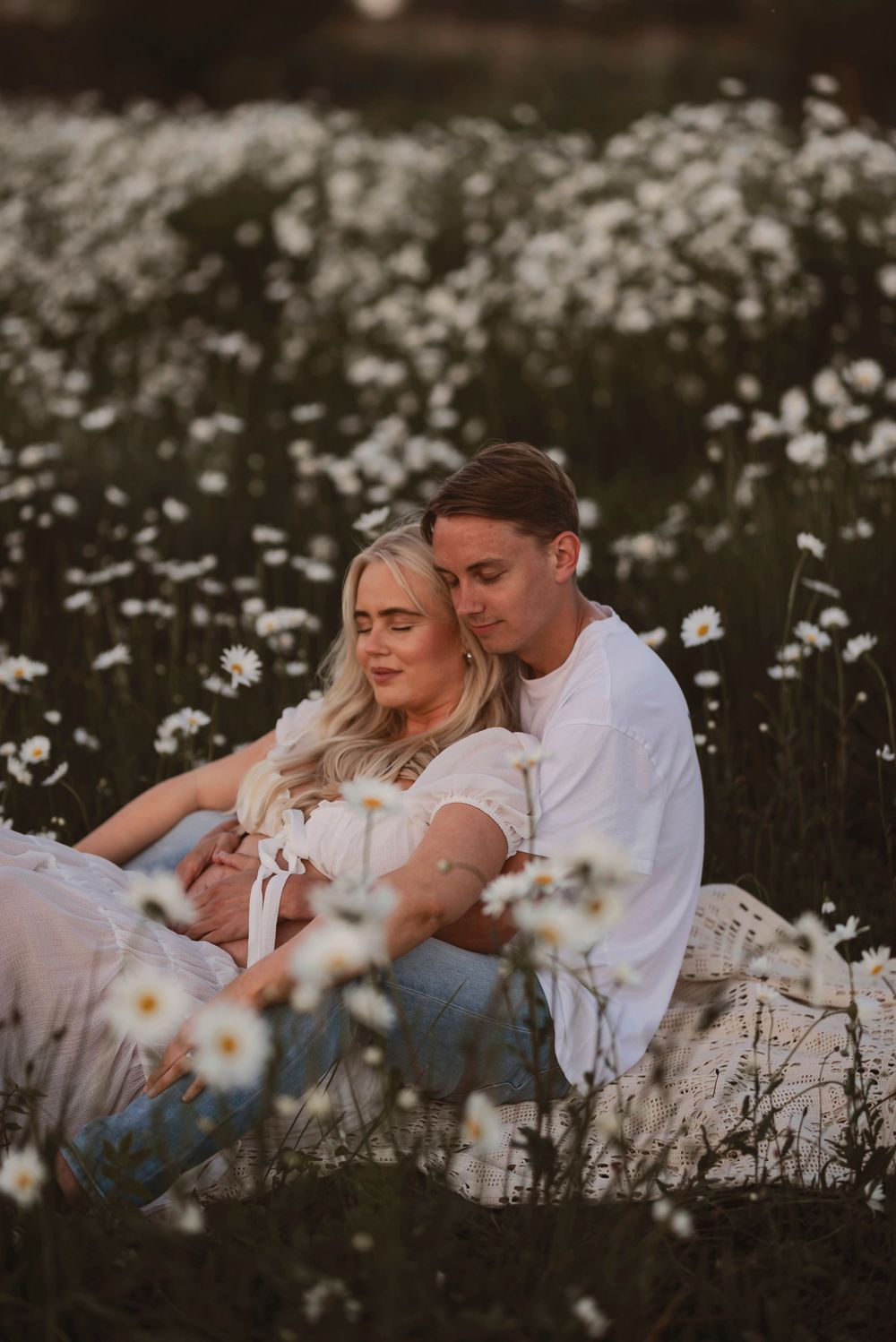 Romantic couple's maternity photos in blooming wildflower meadow with warm sunset glow.