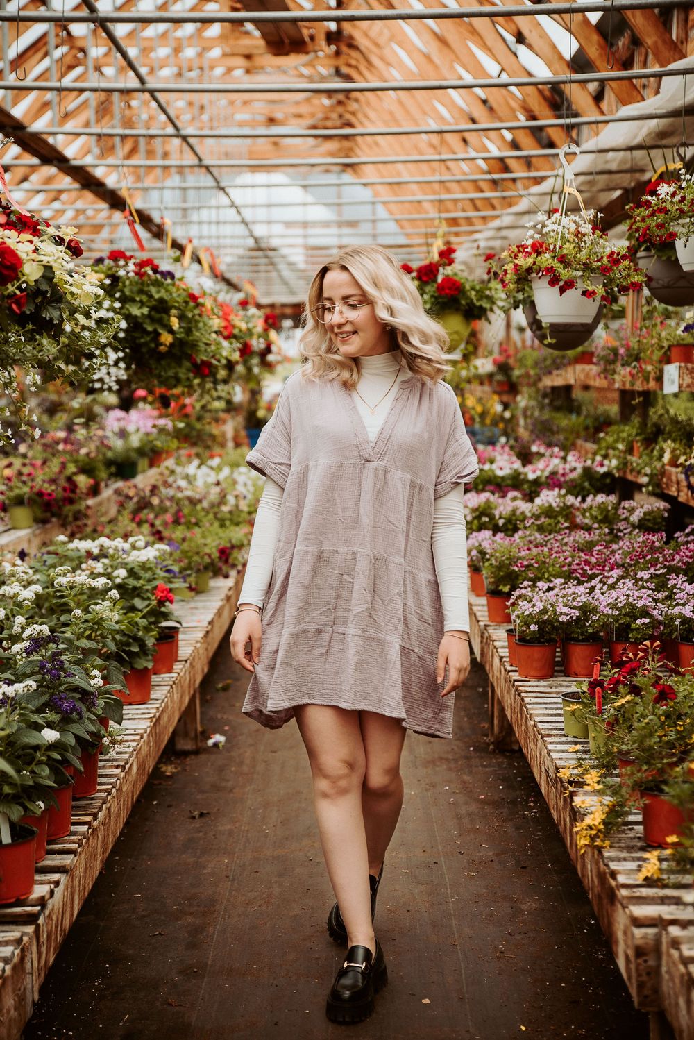Interior of a flower-filled greenhouse with hanging baskets and colorful blooms lining both sides of the walkway.