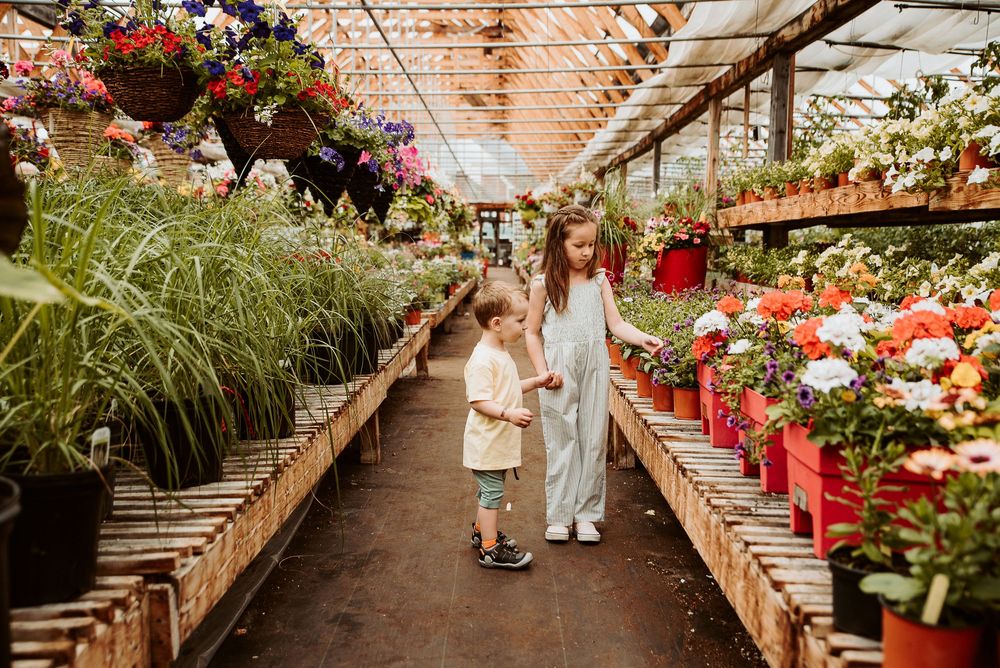 Young girl surrounded by colorful flowers and plants in a bright greenhouse setting.