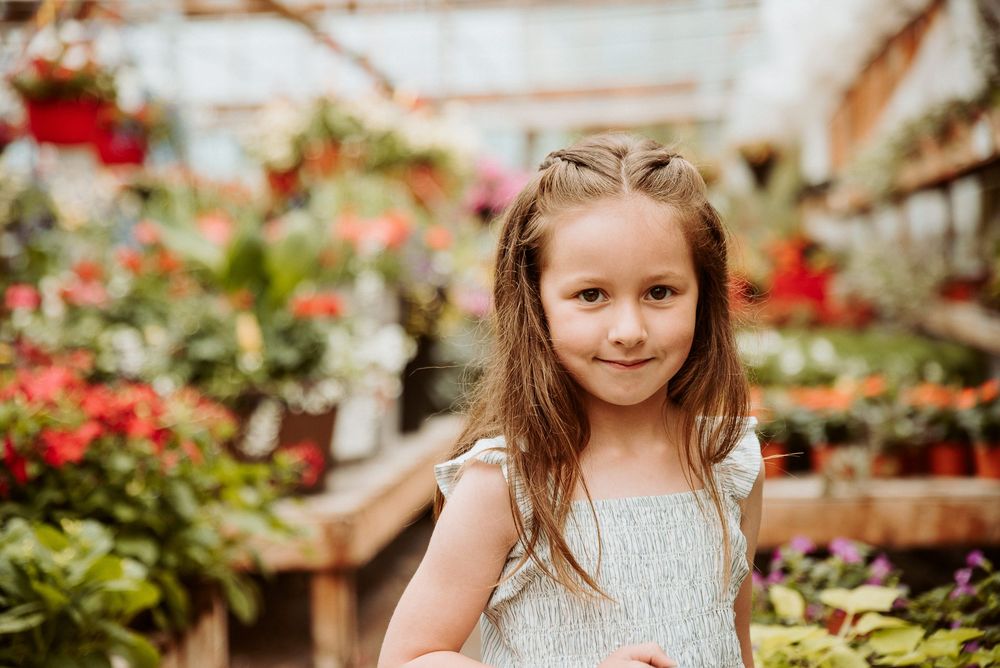 A greenhouse aisle filled with potted plants and flowers on wooden shelving.