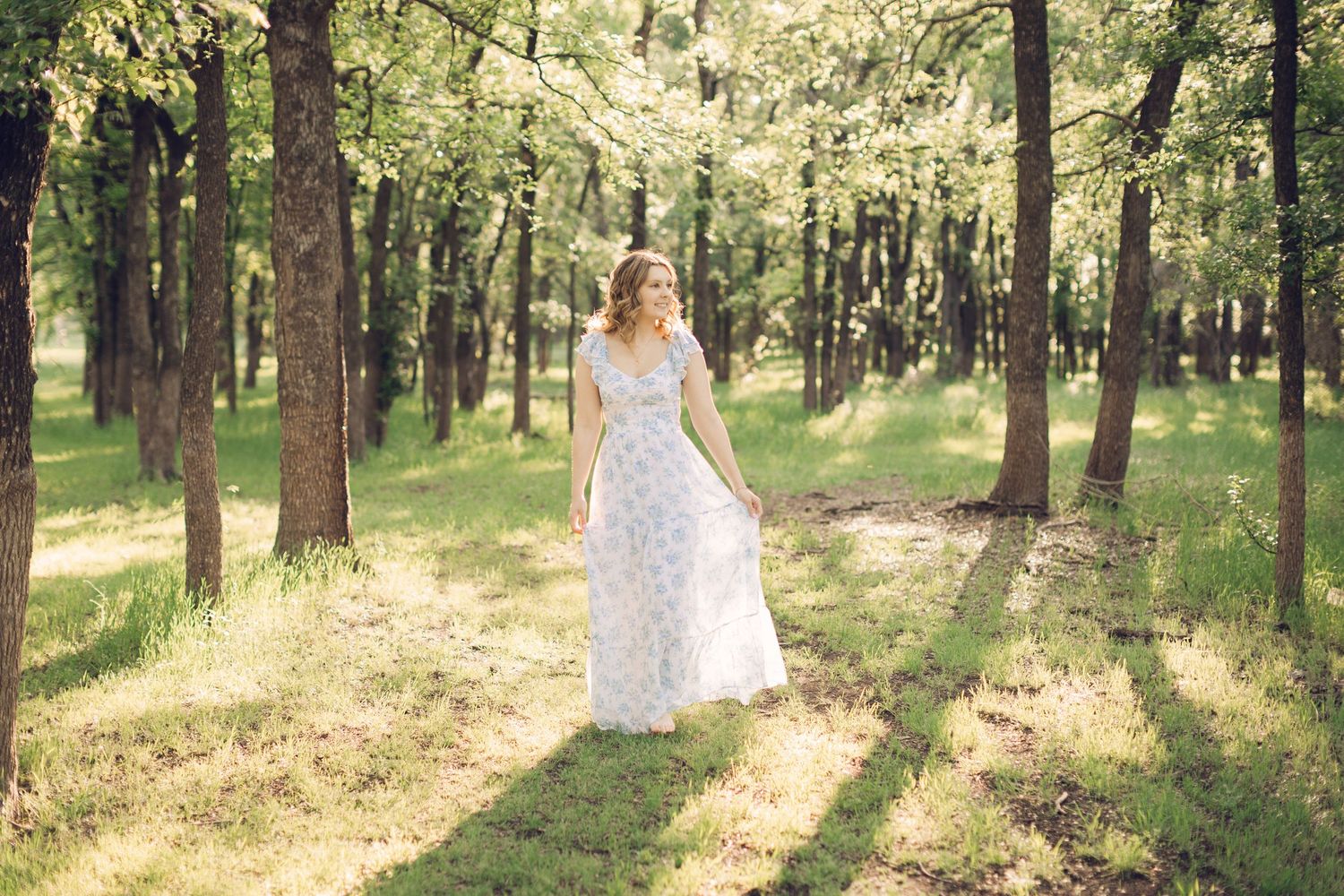 Sunlit forest pathway through tall pine trees creates a natural wedding or senior setting.