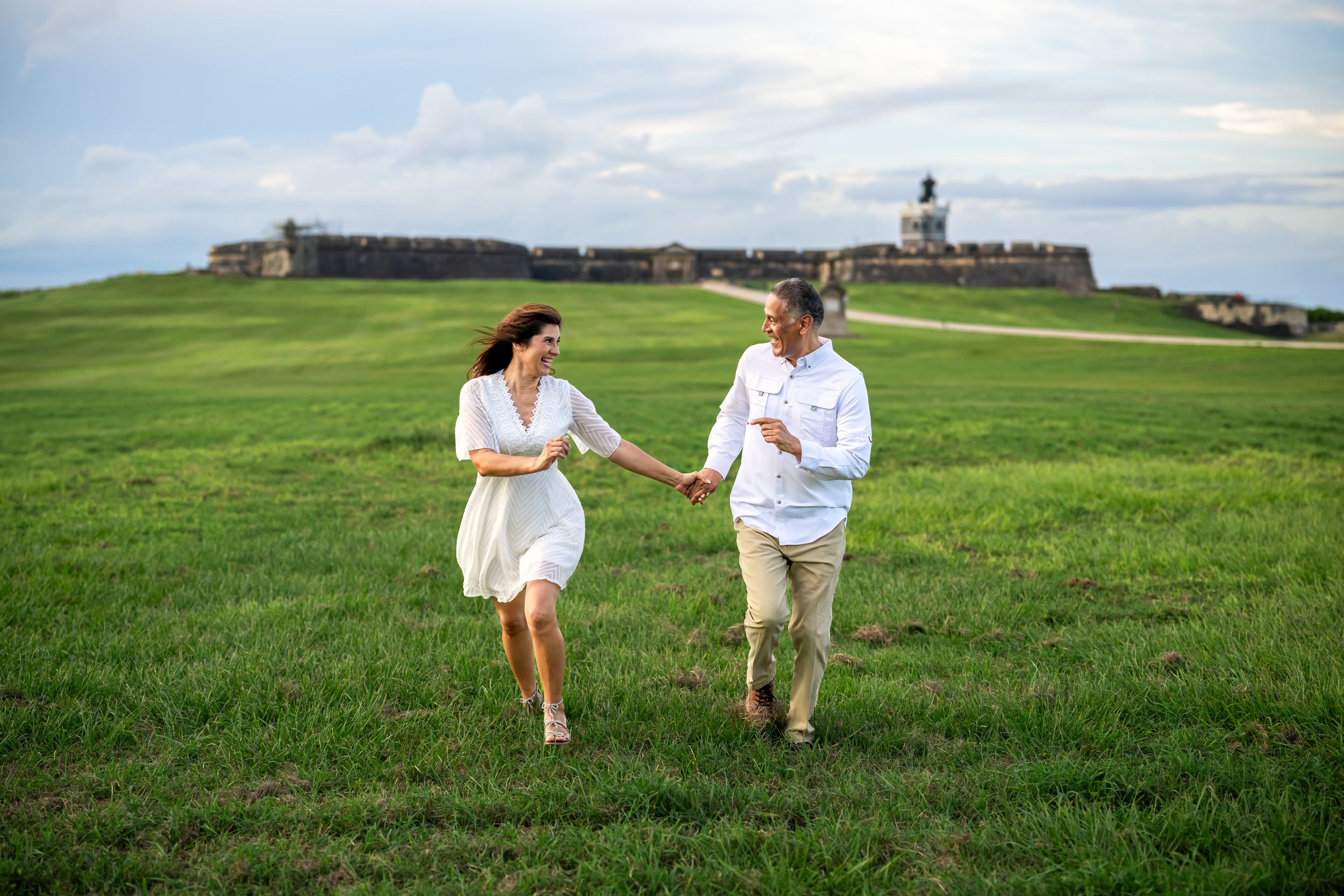 Romantic couple strolls together through green rolling hills under cloudy skies.