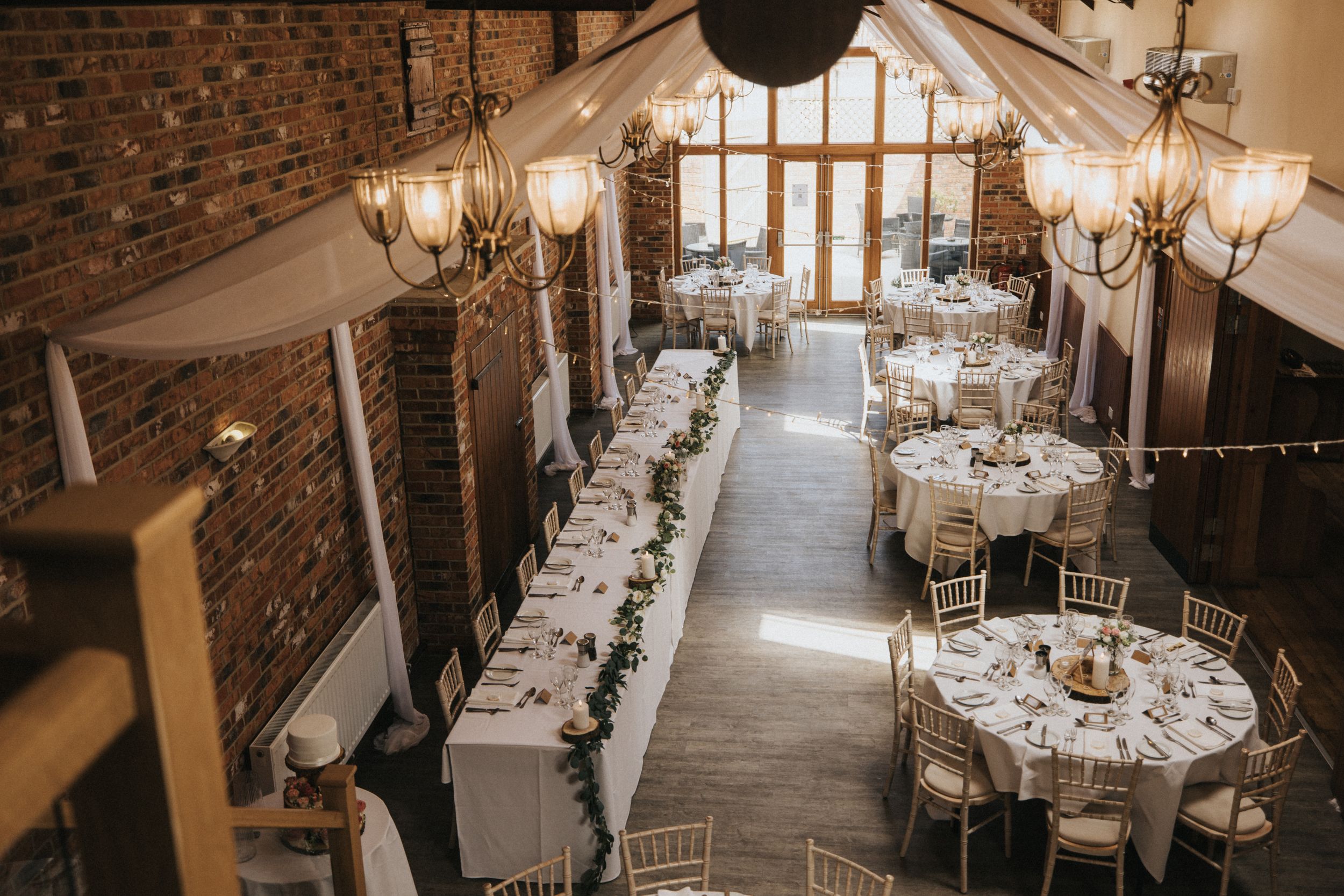 Rustic wedding reception hall with exposed brick walls and elegant chandeliers at Hall Farm - image captured by Grimsby photographers.