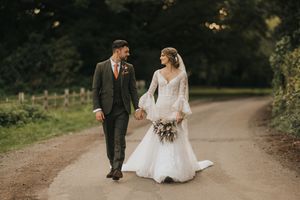 Wedding couple walking through a scenic autumn forest path holding hands at Hall Farm - image captured by Grimsby photographers.