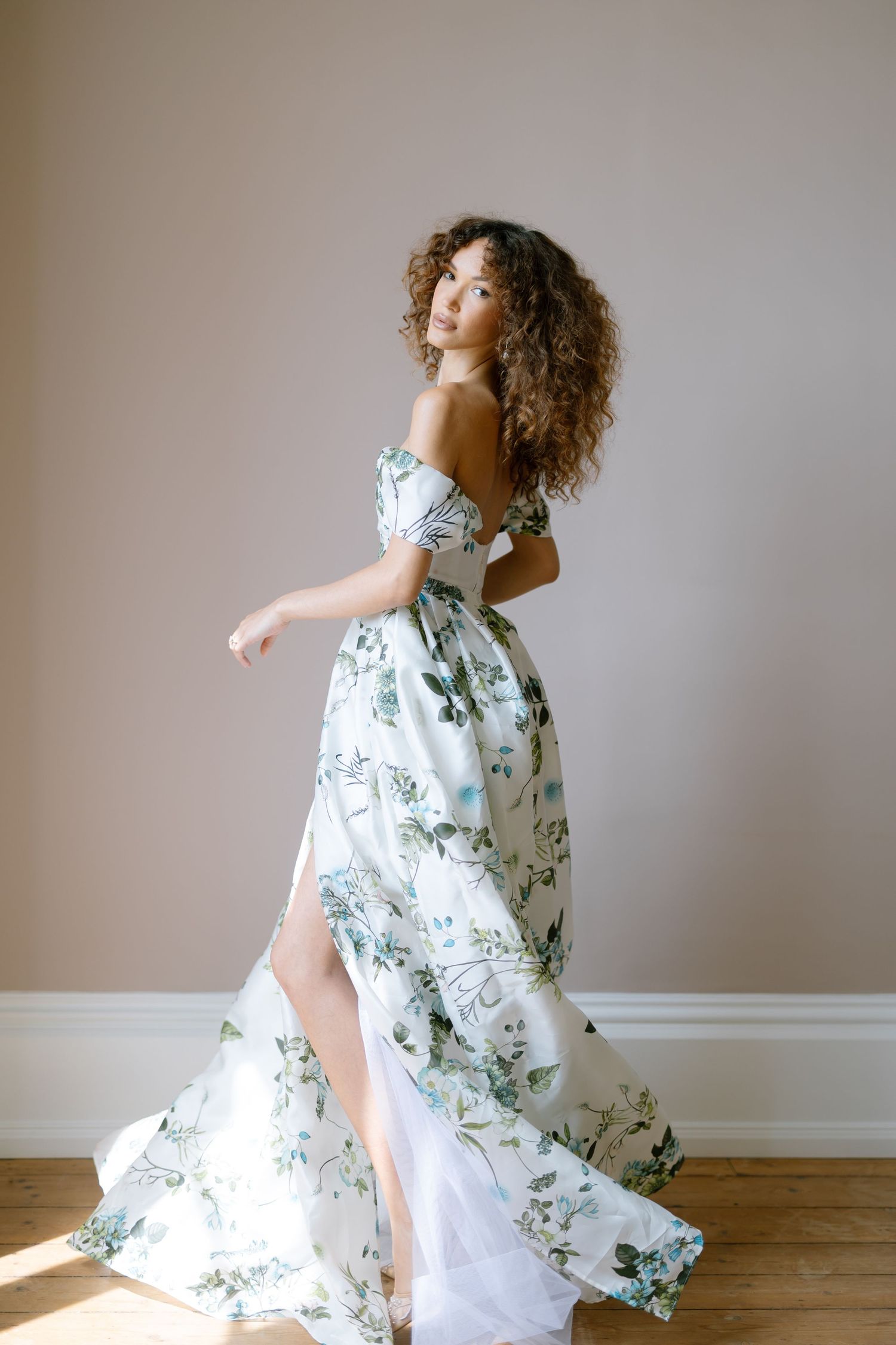 A flowing floral print dress with blue and white patterns creates an ethereal movement effect against a neutral wall.