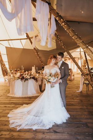 A couple shares a romantic moment on a wooden dance floor under twinkling lights and draped fabric at Nuddock Wood Lake.