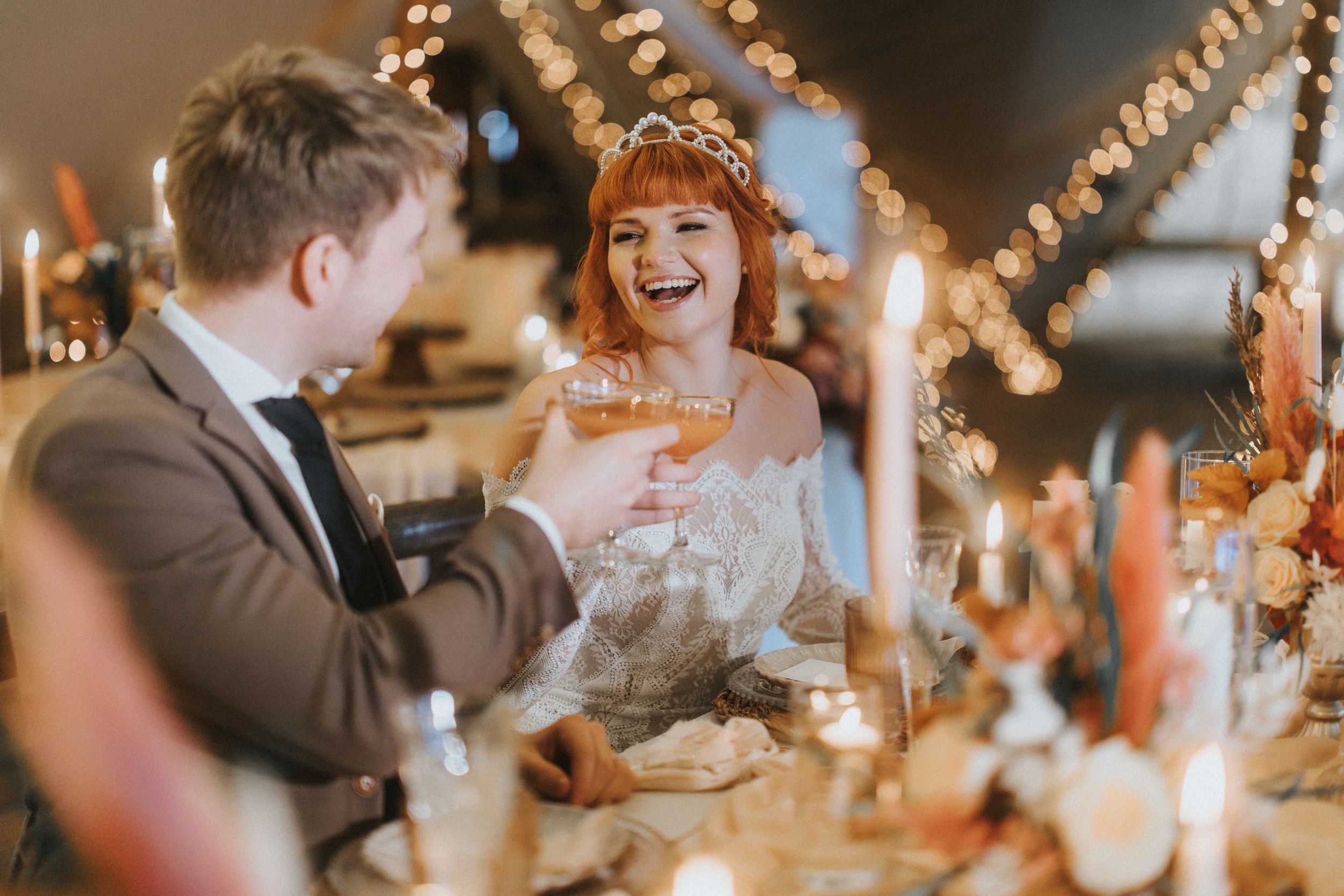 A couple shares a warm moment at their wedding reception table surrounded by glowing string lights and candles at Nuddock Wood Lake.