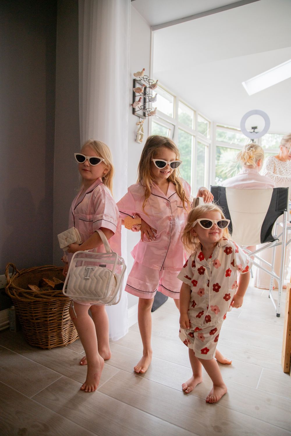 Three children in pink pajamas and sunglasses pose confidently indoors.