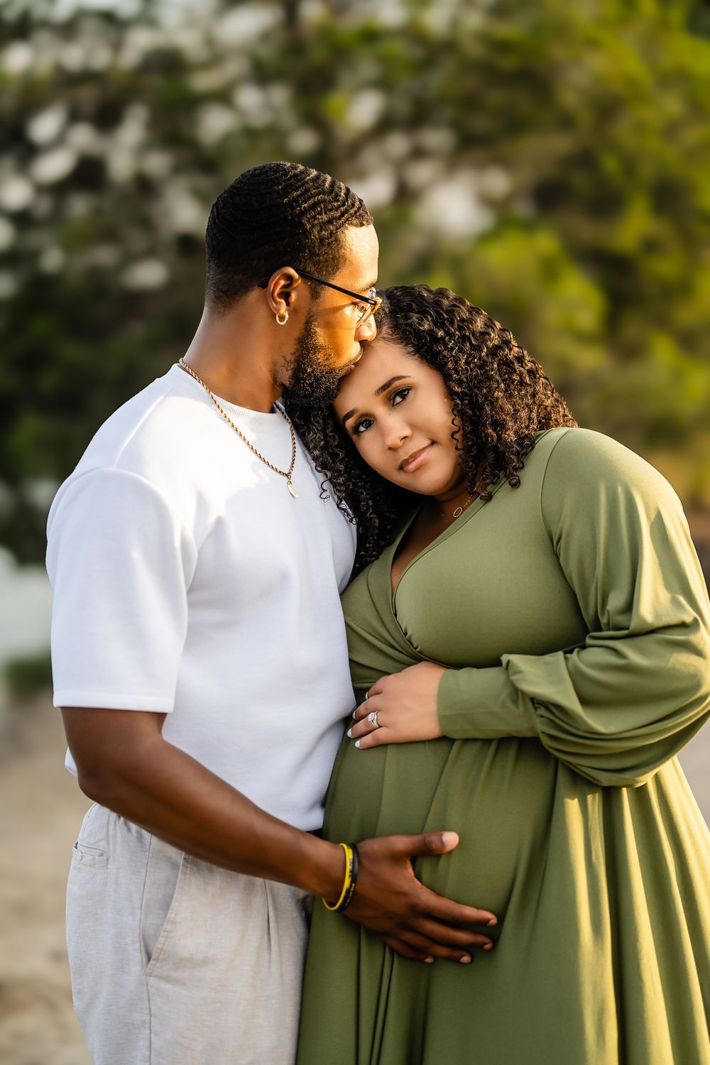 A couple shares a tender embrace outdoors, with one person wearing white and the other in olive green attire.