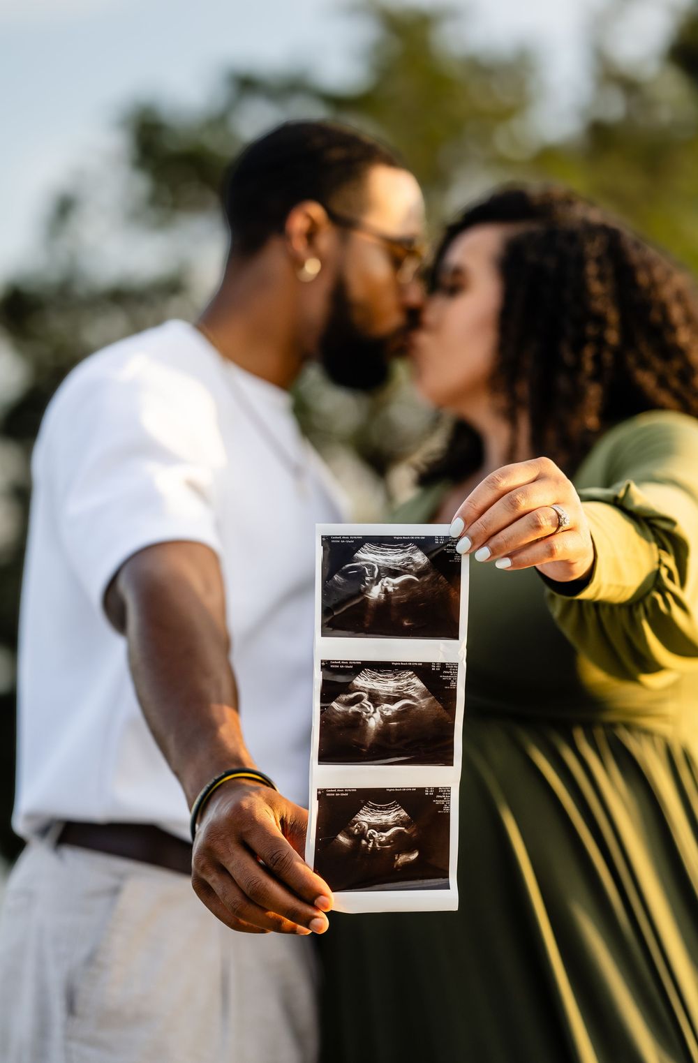 Couple holding ultrasound photos during sunset pregnancy announcement photoshoot in outdoor setting.
