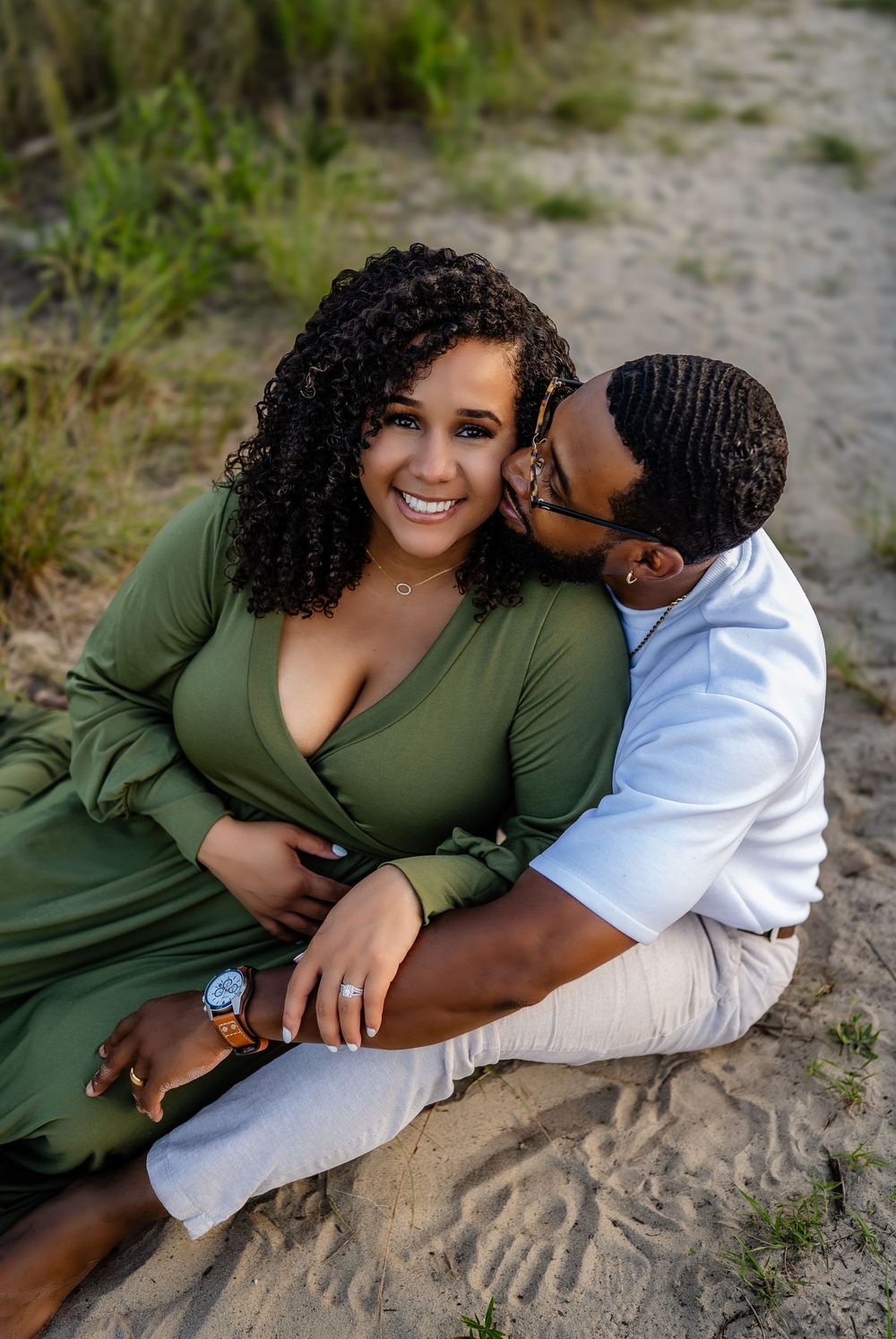 A loving couple in casual attire sharing an intimate moment while sitting together on sandy ground outdoors.